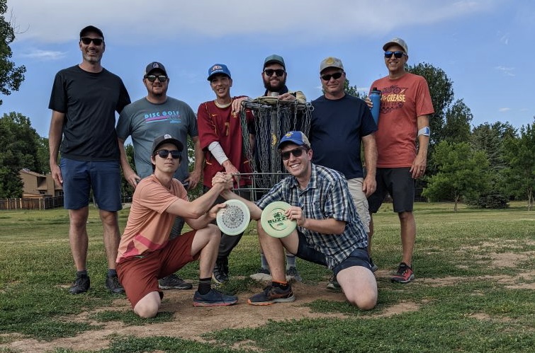 Photo of eight people posing around a disc golf basket